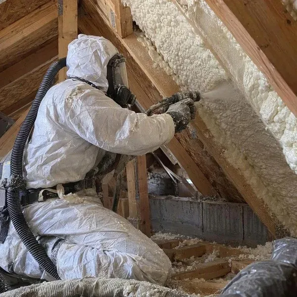 Installer spraying closed cell foam between tight attic rafters