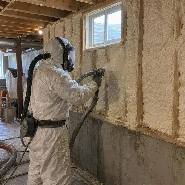 Installer spraying foam on a basement wall beside a window